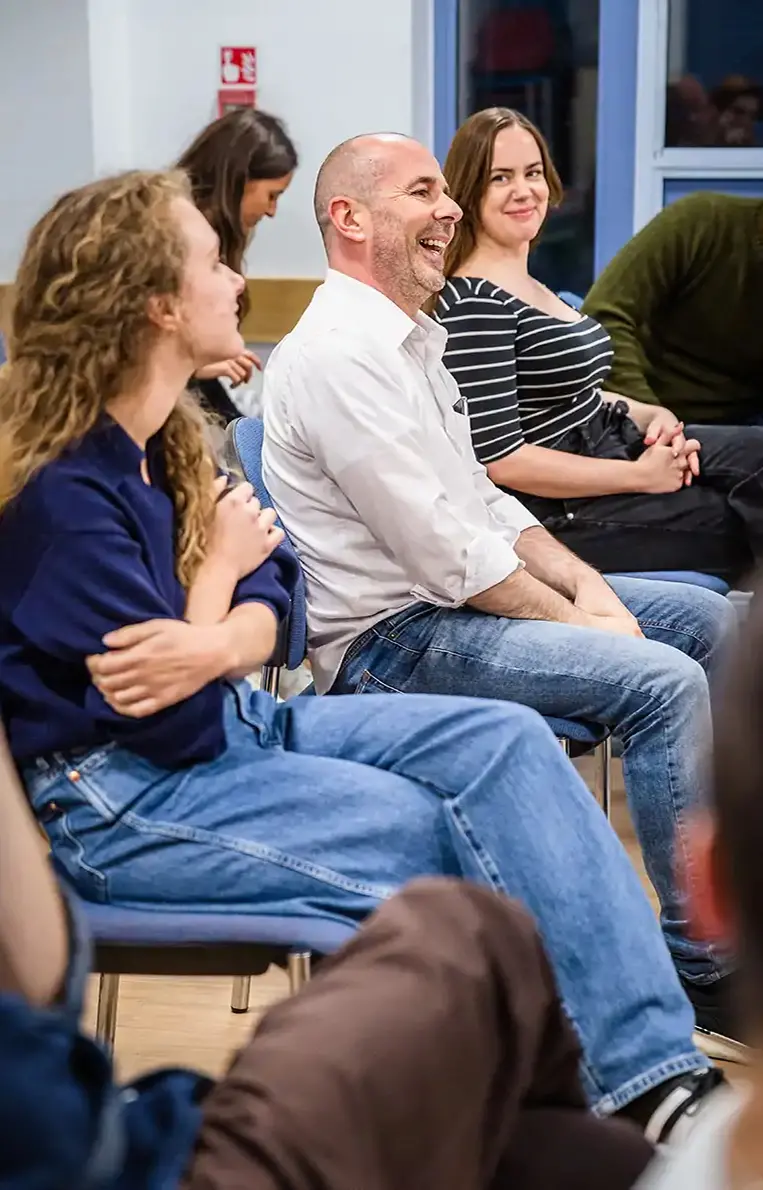 Group of adults sitting in chairs, smiling and engaged in a discussion in a bright room.