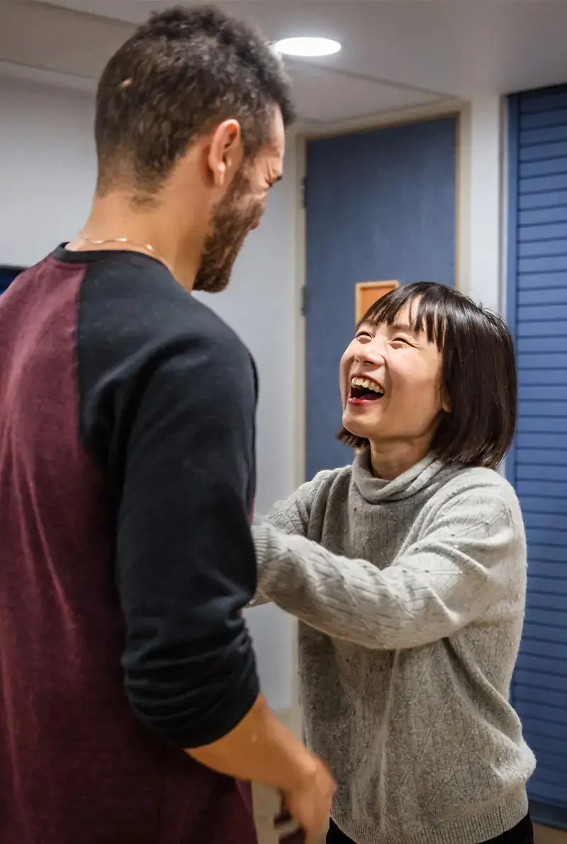 Laughing woman in gray sweater holding the arms of a smiling man wearing a black and maroon shirt.