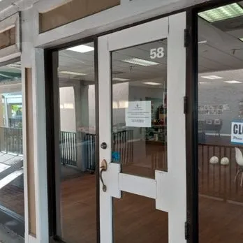 Glass storefront door with the number 58 and a sign on it, showing interior with wooden floor and a railing.