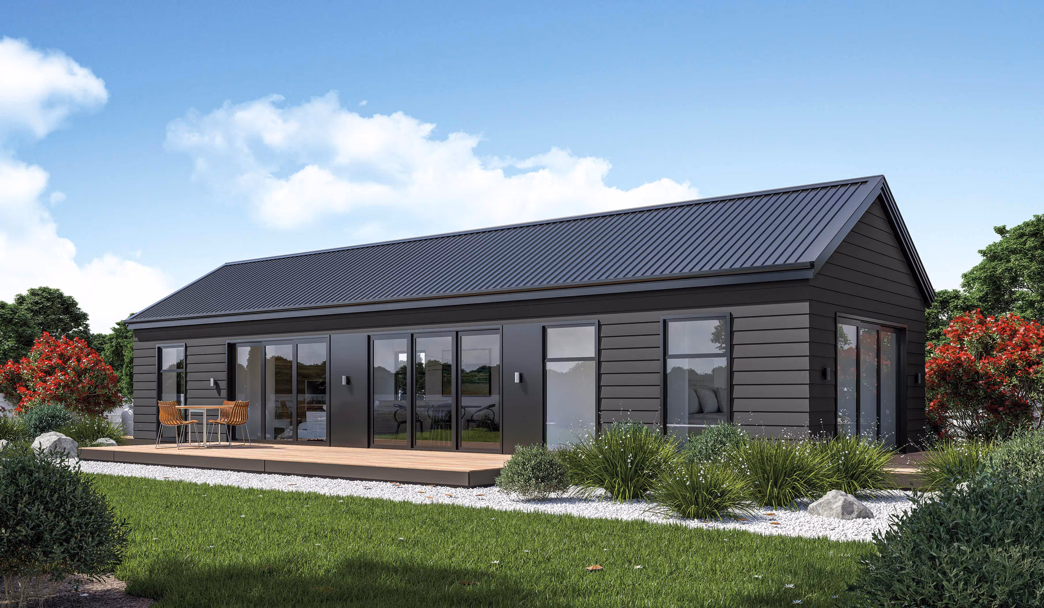 Modern single-story black house with a metal roof, large glass doors, wooden deck, and surrounding greenery and flowering bushes.