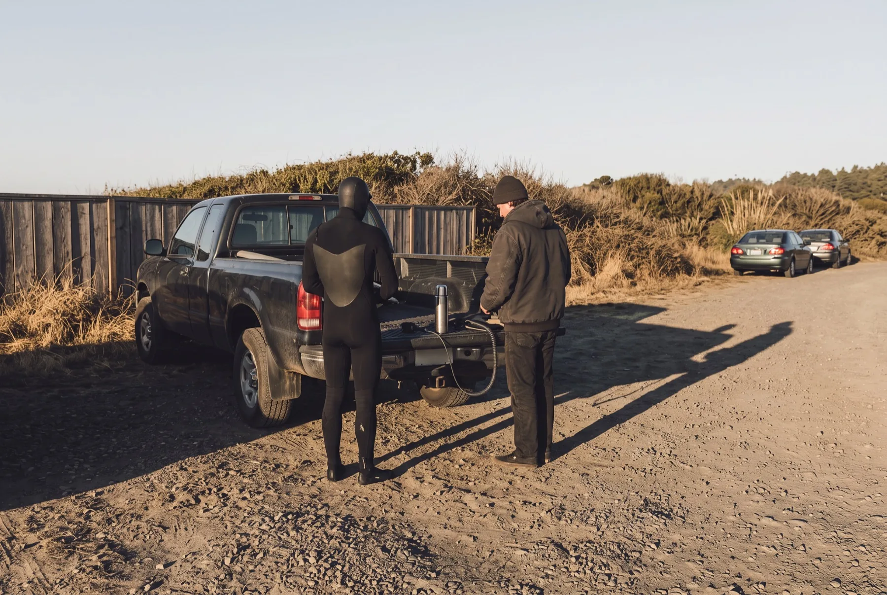 Two figures at a tailgate in a dirt pullout at first light