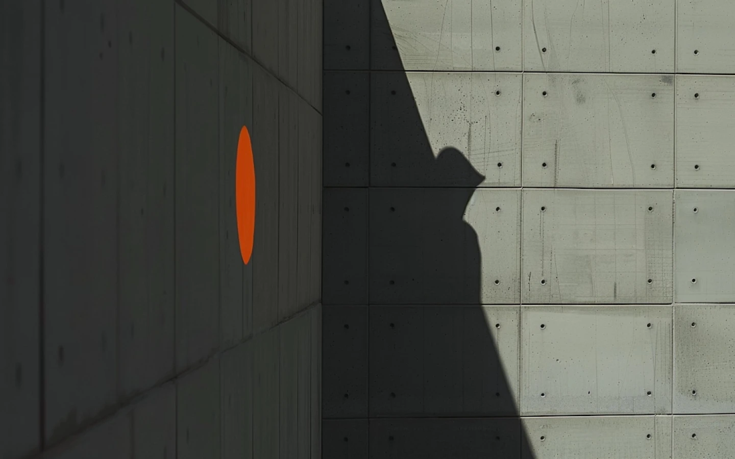 Concrete building facade with a single bright orange circular window casting a shadow.