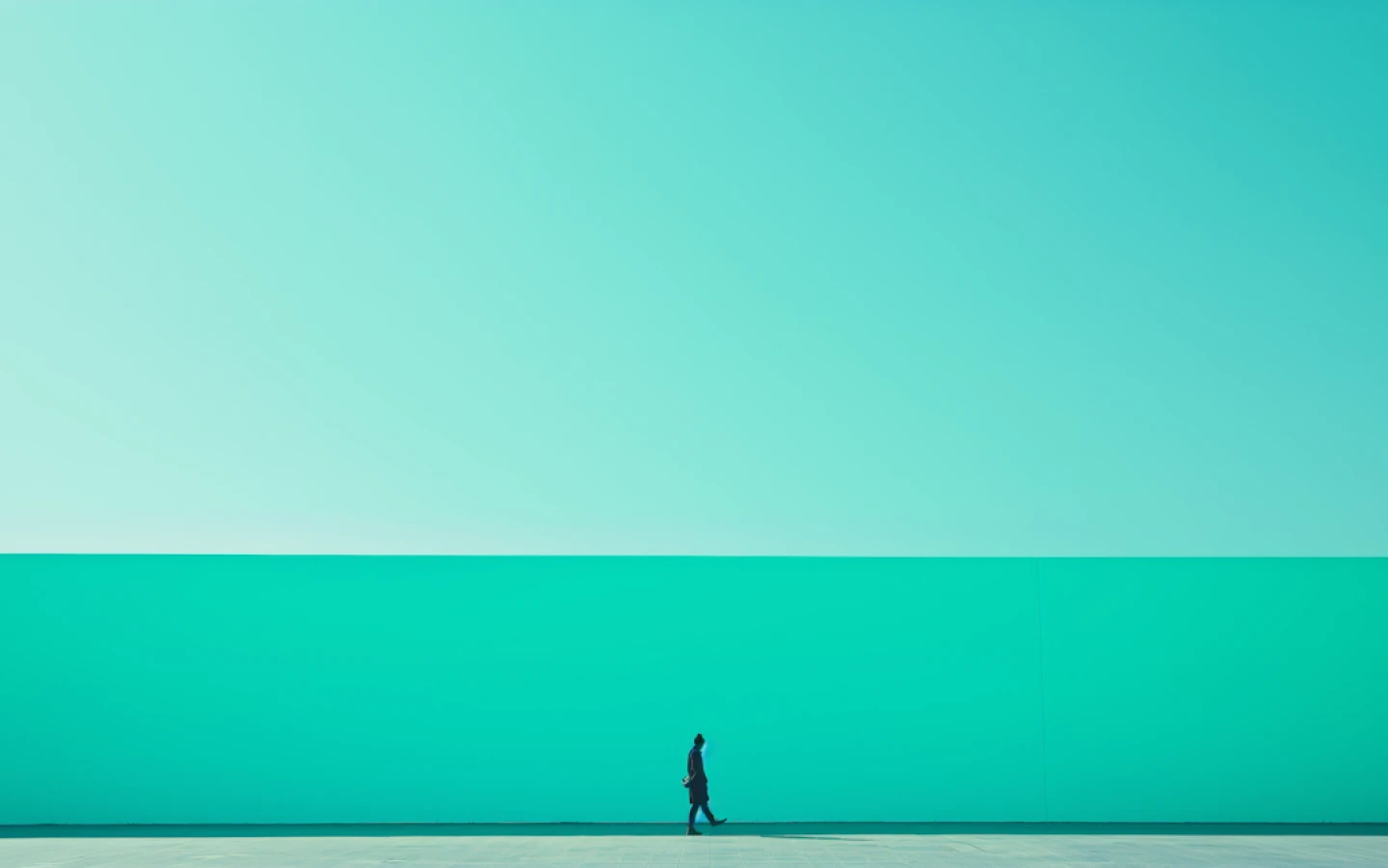 Person standing alone near the horizon in front of a bright turquoise sky and sea.