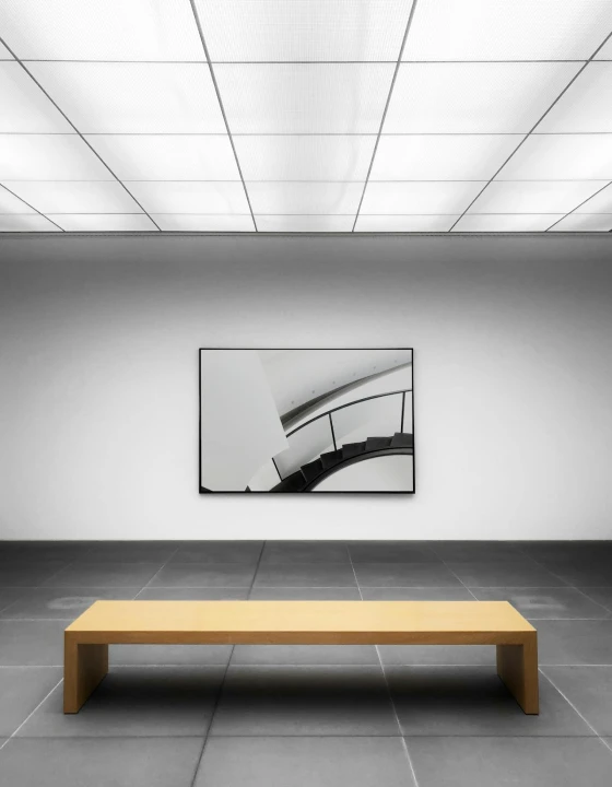Clean gallery room with a framed artwork on the wall and a wooden bench beneath it.
