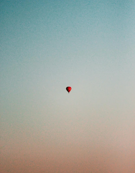 A single red balloon drifting in a gradient sky from blue to orange.