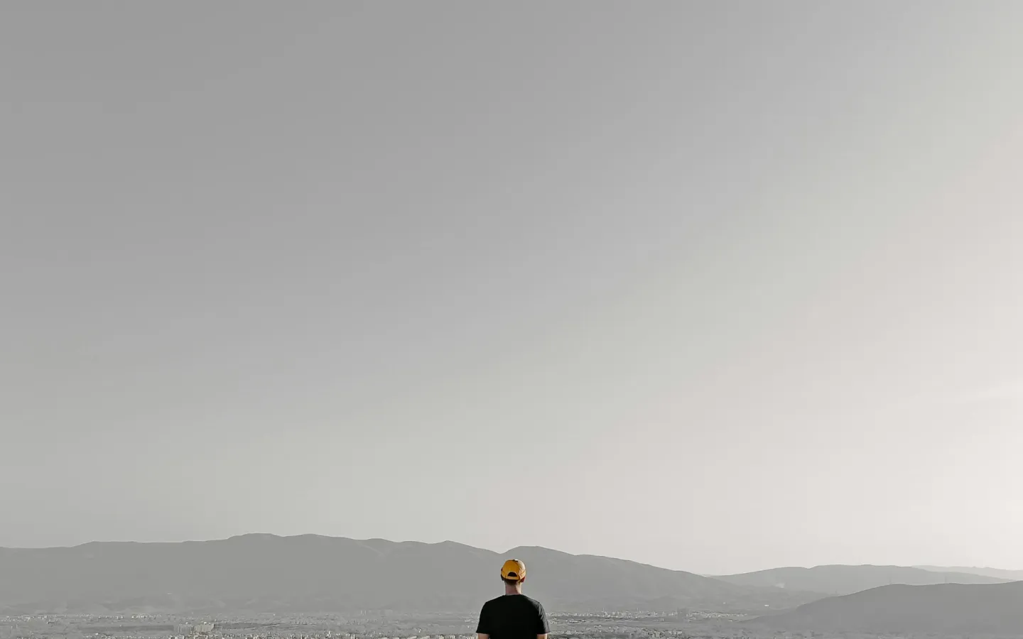 Silhouette of a person standing by a calm lake under an overcast sky.