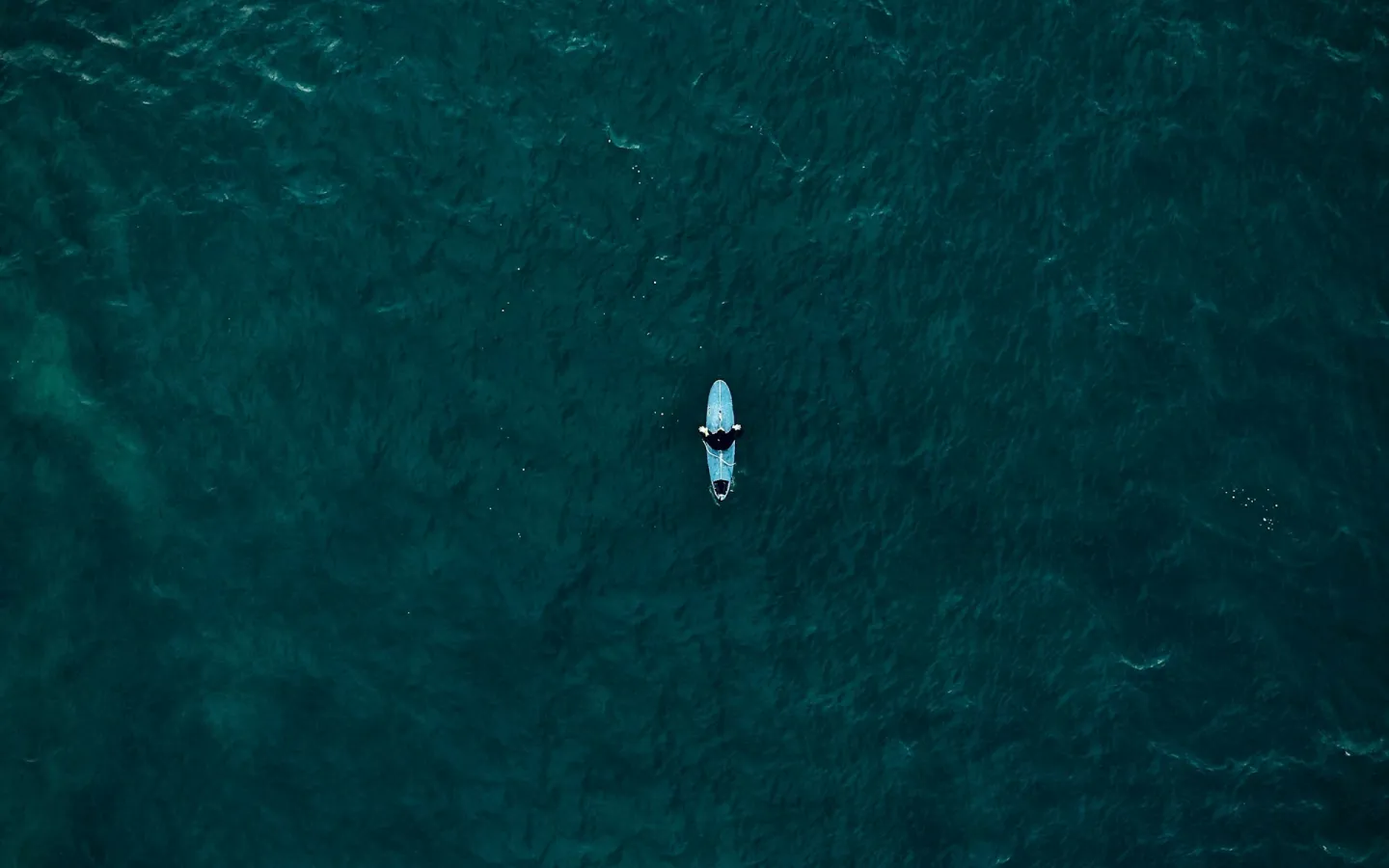 Aerial shot of a lone surfer in the middle of a deep green-blue ocean.