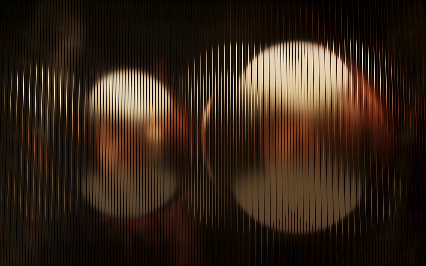 Two large warm-toned circular lights seen through vertical textured glass panels.