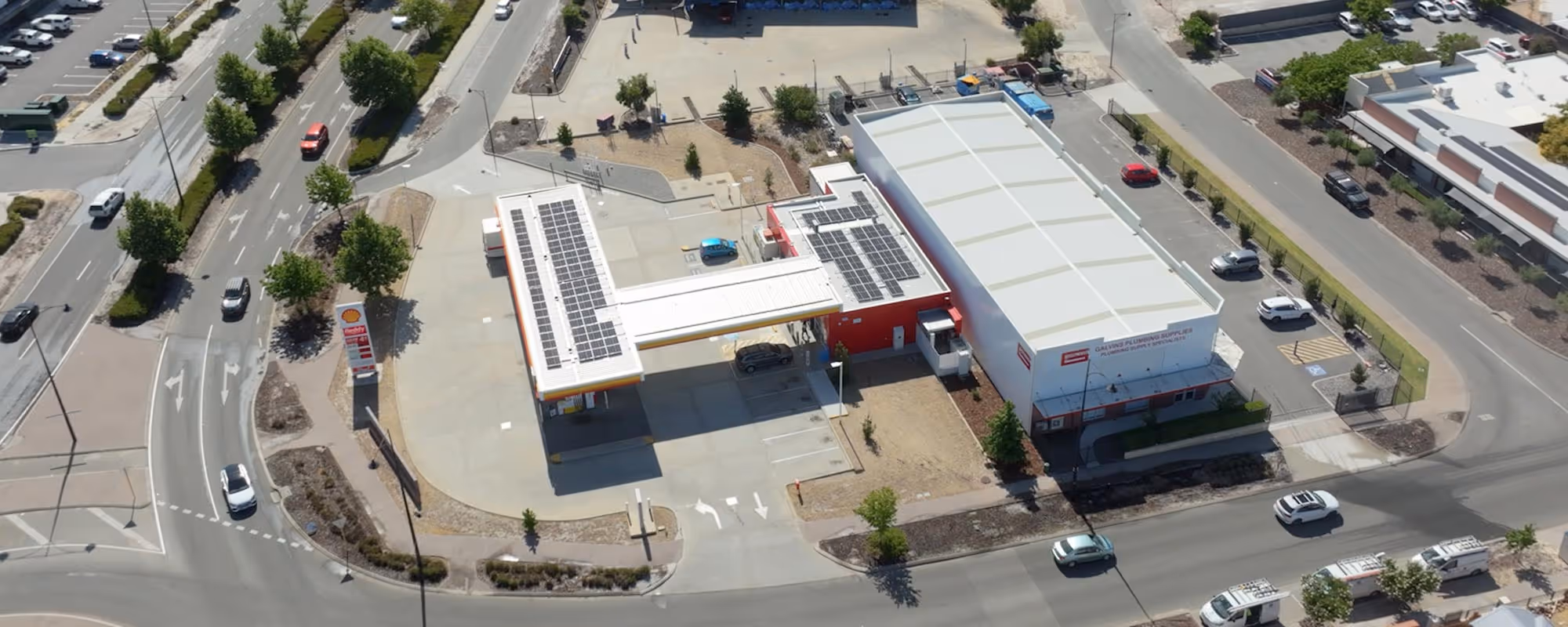 Aerial view of a gas station with solar panels on the roof next to a plumbing supply warehouse with parking spaces.