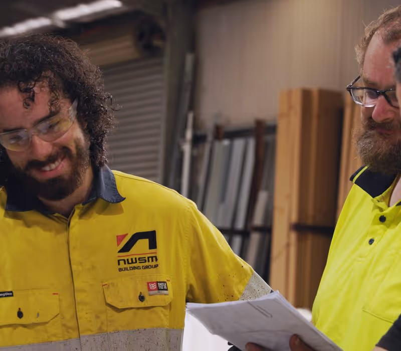 Two men in yellow work shirts reviewing papers inside a workshop or warehouse.