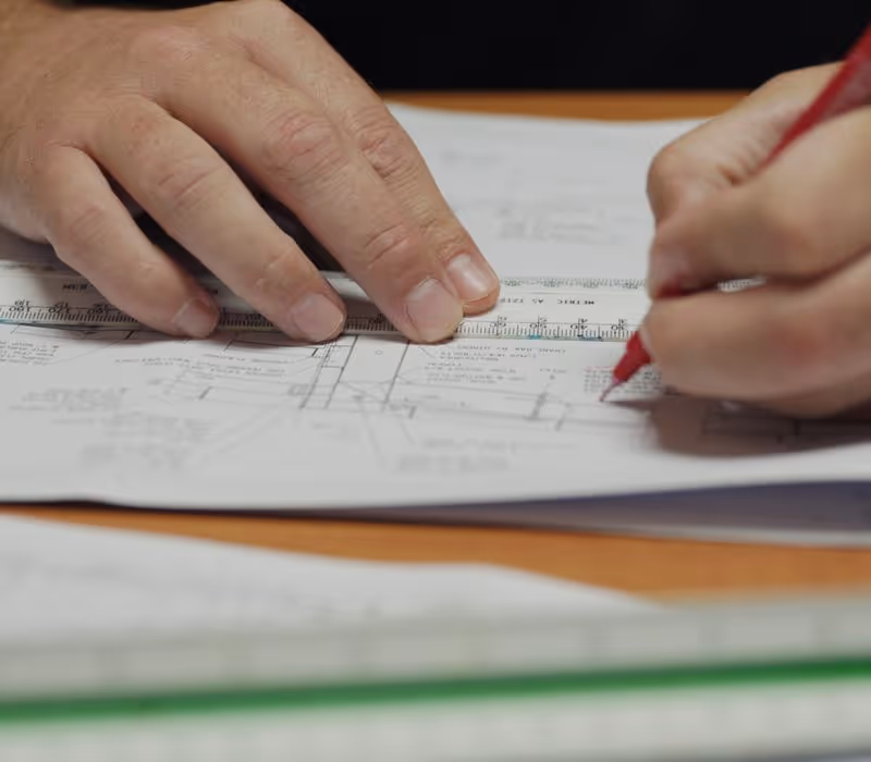 Close-up of hands using a ruler and red pen to mark measurements on architectural plans.