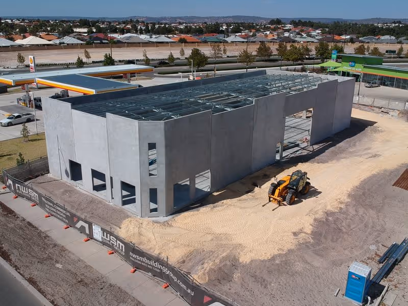 Commercial building under construction near a Shell gas station with heavy machinery on sandy ground.