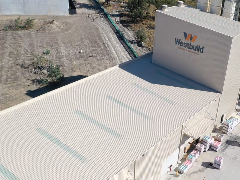 Aerial view of a large beige Westbuild warehouse with materials stacked outside on concrete ground.