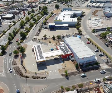 Aerial view of a gas station with solar panels on the roof beside a busy road and parking areas.