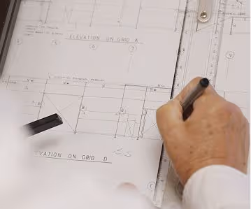 Person drawing architectural blueprints using a pen and ruler on detailed plans.