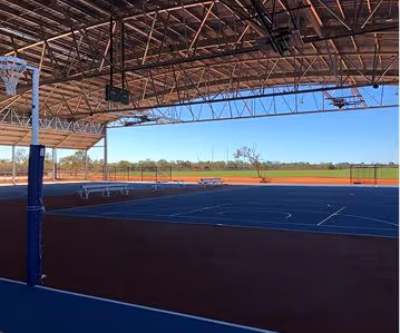 Covered outdoor basketball court with blue playing surface and a basketball hoop on the left.