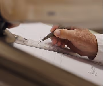 Hand holding a pen and drawing precise lines on a paper using a ruler.