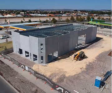 A large rectangular building under construction with concrete walls and machinery nearby.