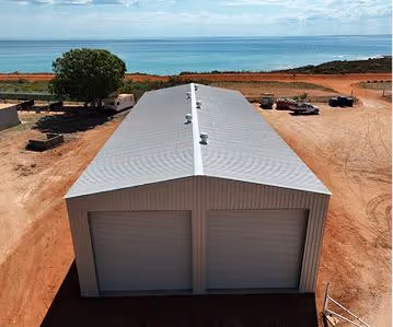 Large gray metal storage building with two closed garage doors on a dirt lot near the ocean.
