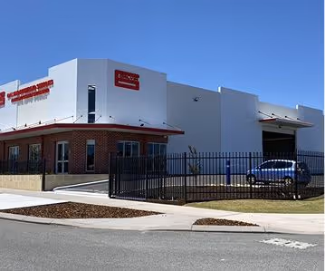 Modern warehouse with brick and white walls, black fence, and parked blue car under clear sky.