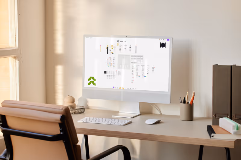 Modern minimalist workspace with a computer displaying a flowchart on a light wood desk, beige chair, and stationery holder.