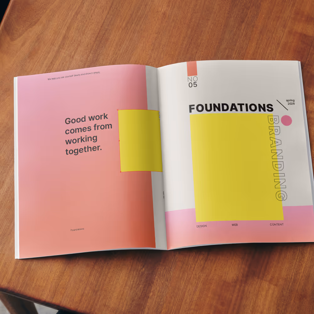 Open magazine on wooden table with a pink-themed page stating 'Good work comes from working together' and a white page titled 'Foundations Branding' with yellow and pink graphic blocks.