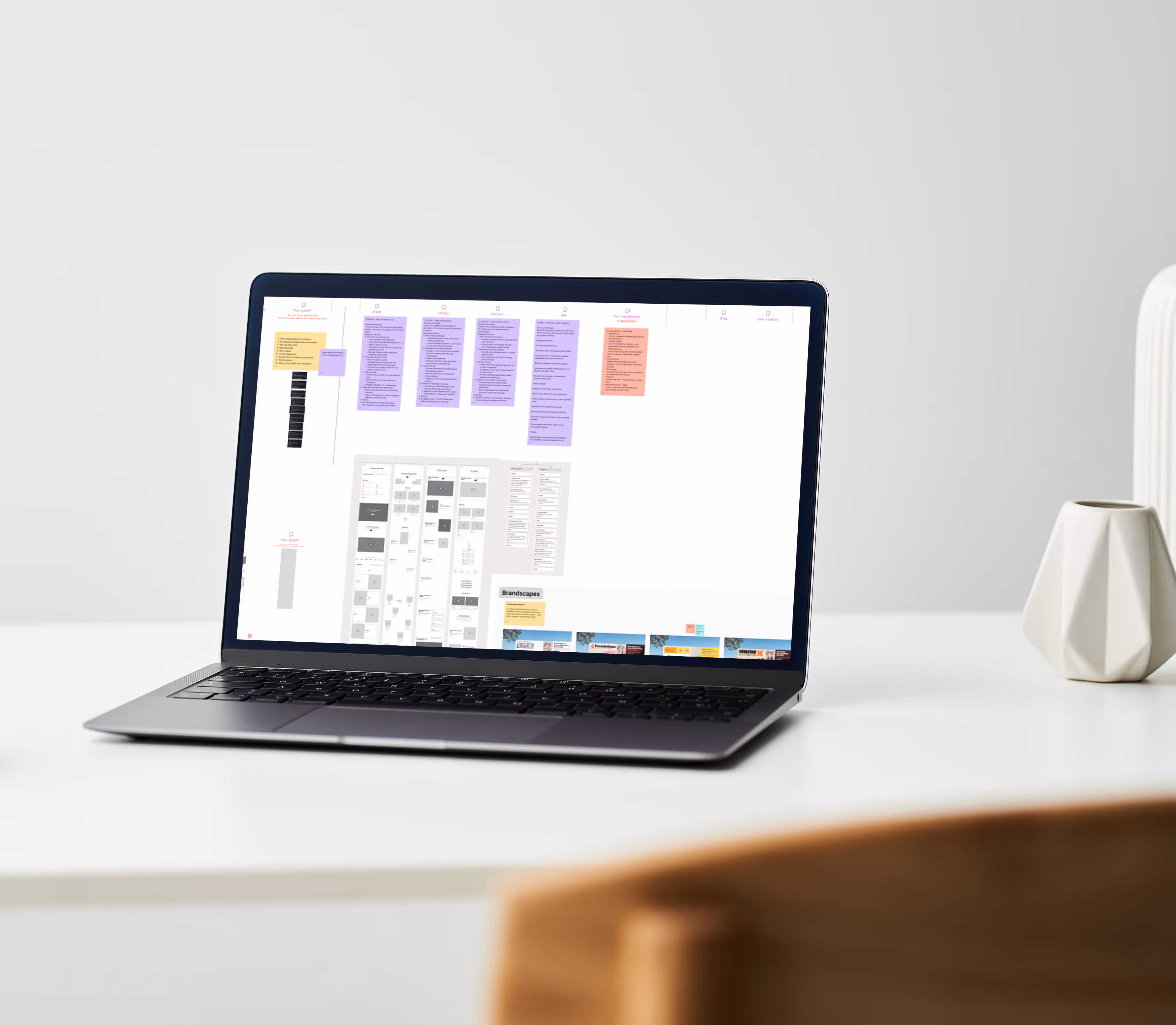 Open laptop displaying a workflow or project plan on a white desk next to a white geometric vase.
