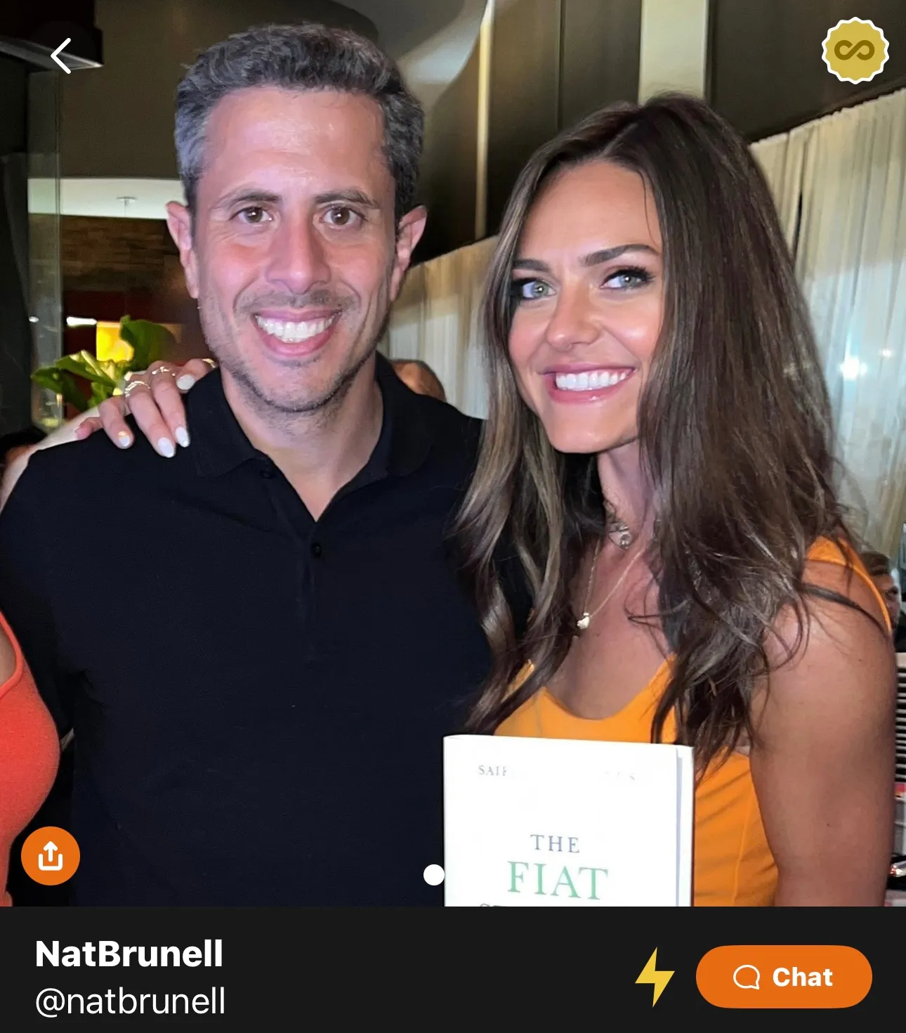 Man and woman smiling together, the woman is holding a book titled 'The Fiat'.