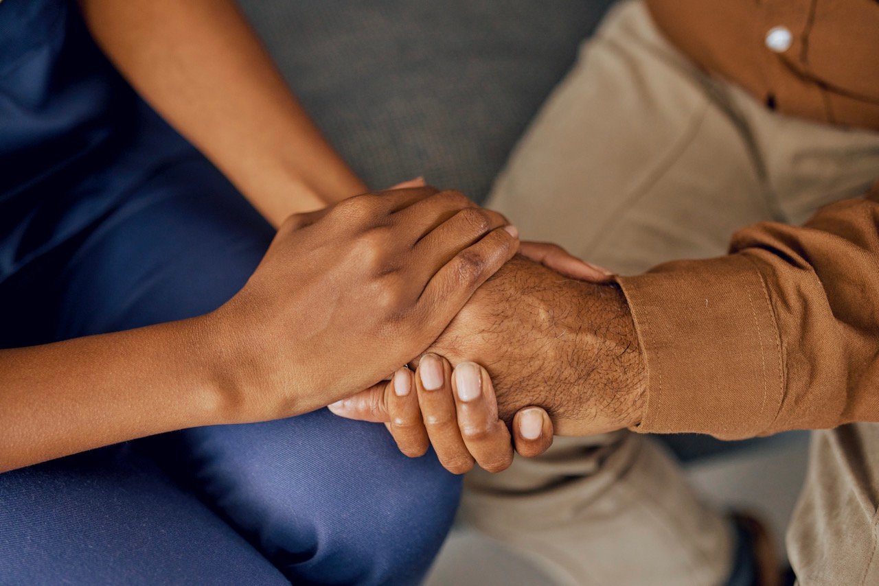 Close-up of two people holding hands, conveying support and compassion.