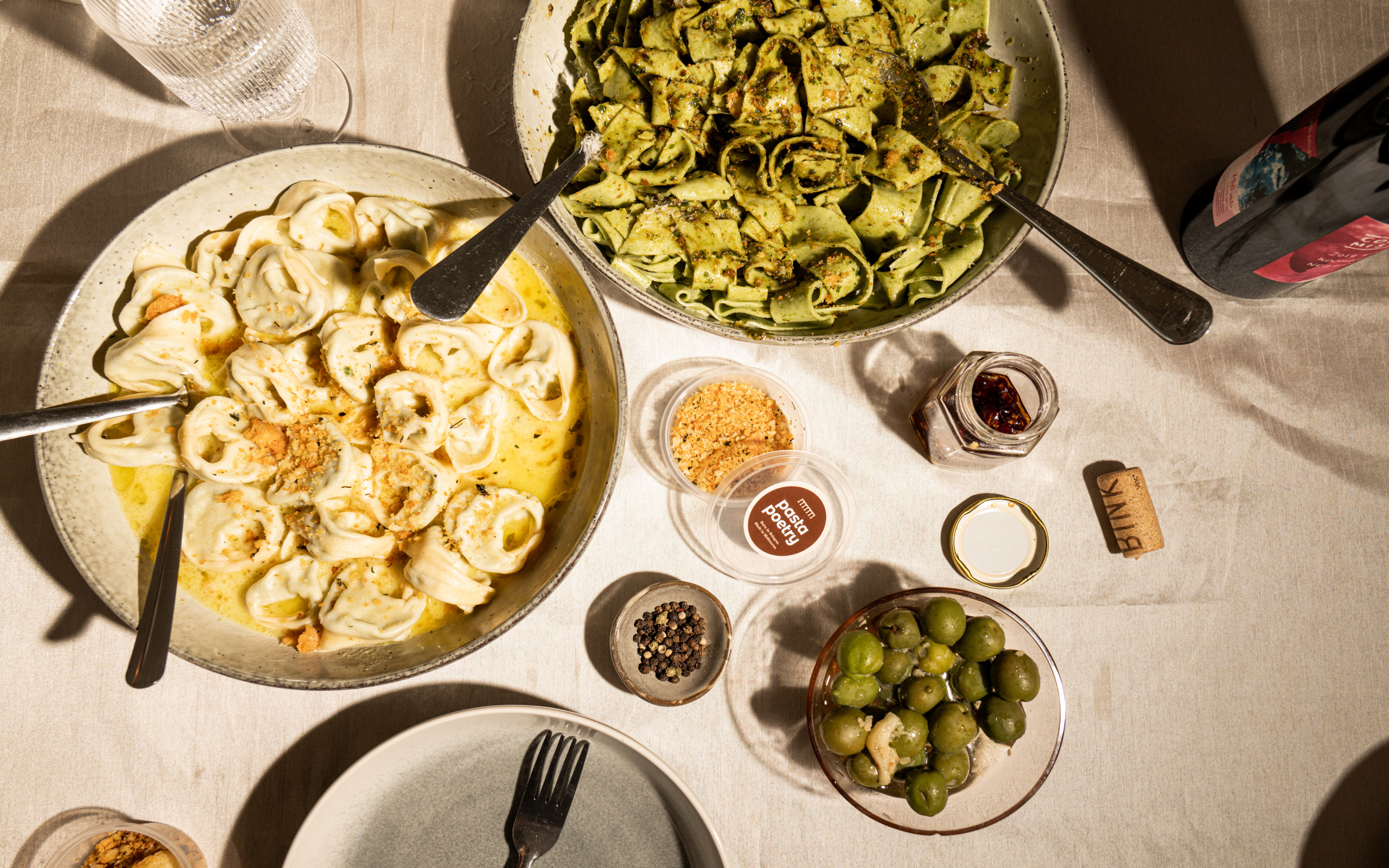 Top-down table setting with bowls of pasta and olives.