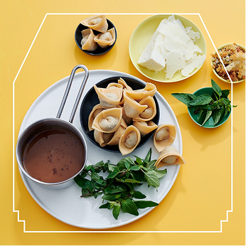 Table setting on yellow surface, with bowl of pasta and associated mise en place. There is a white lined frame over the image.