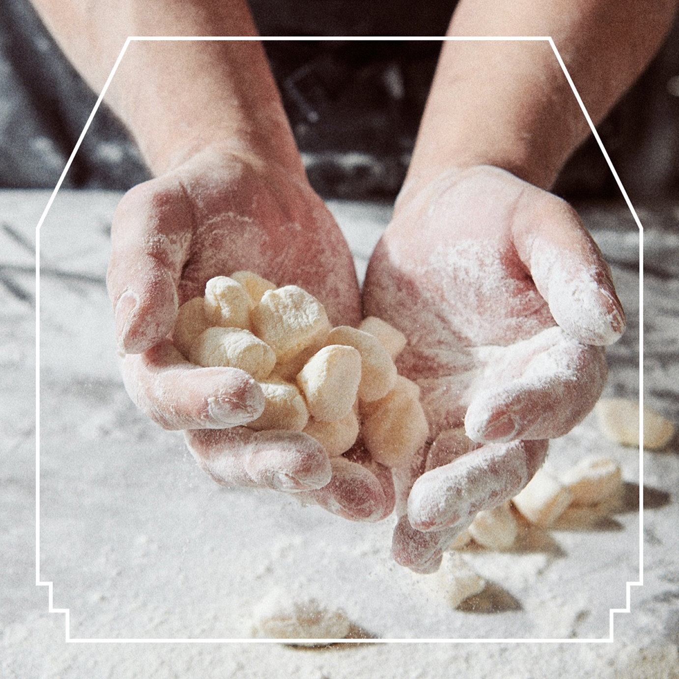 Hands holding floury gnocchi over a floured surface. There is a white lined frame over the image.