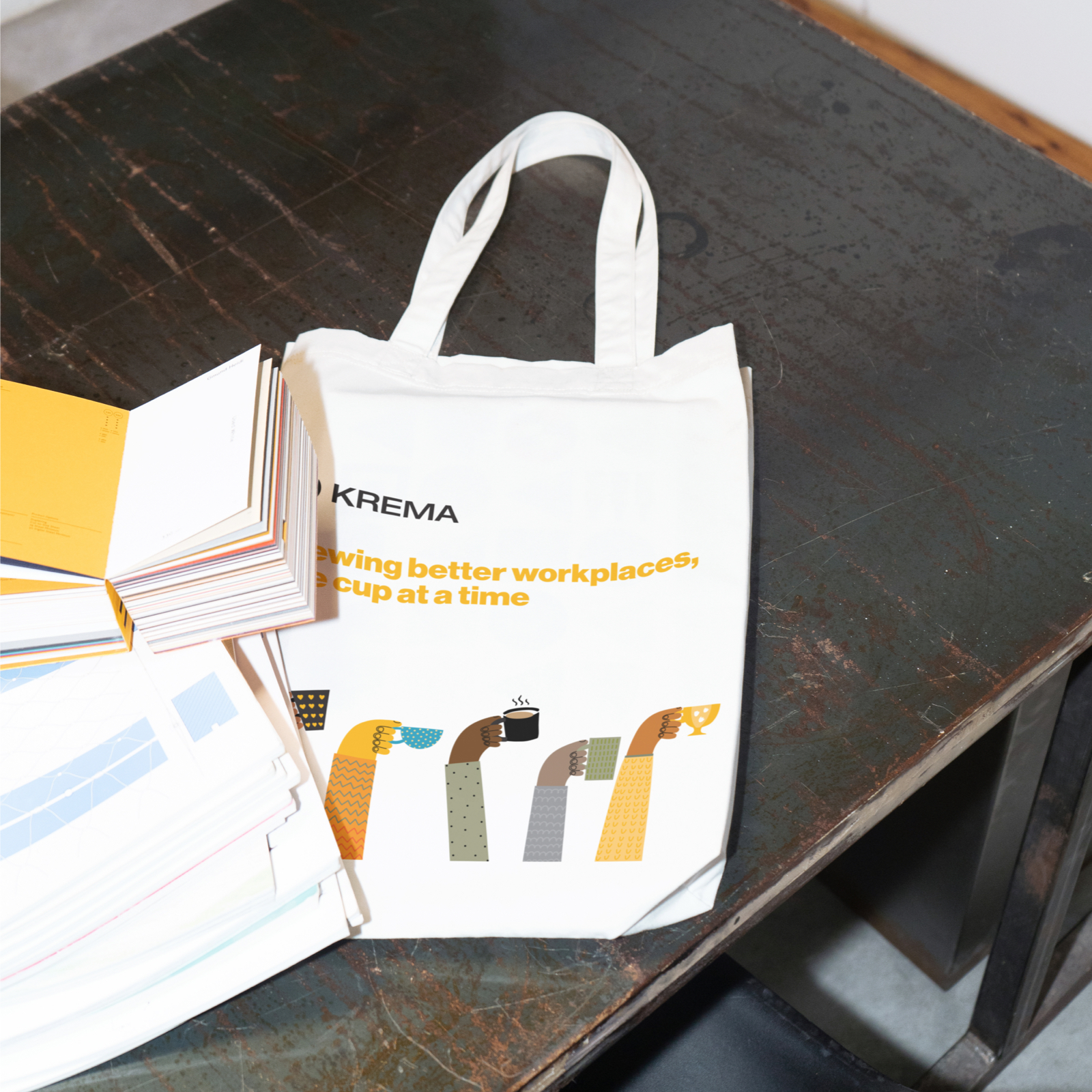White tote bag with Krema logo and illustrated hands holding coffee cups.