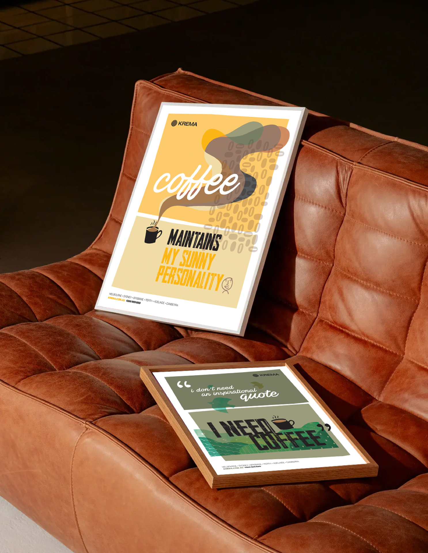 Two Krema posters in frames, scattered on a brown leather couch.