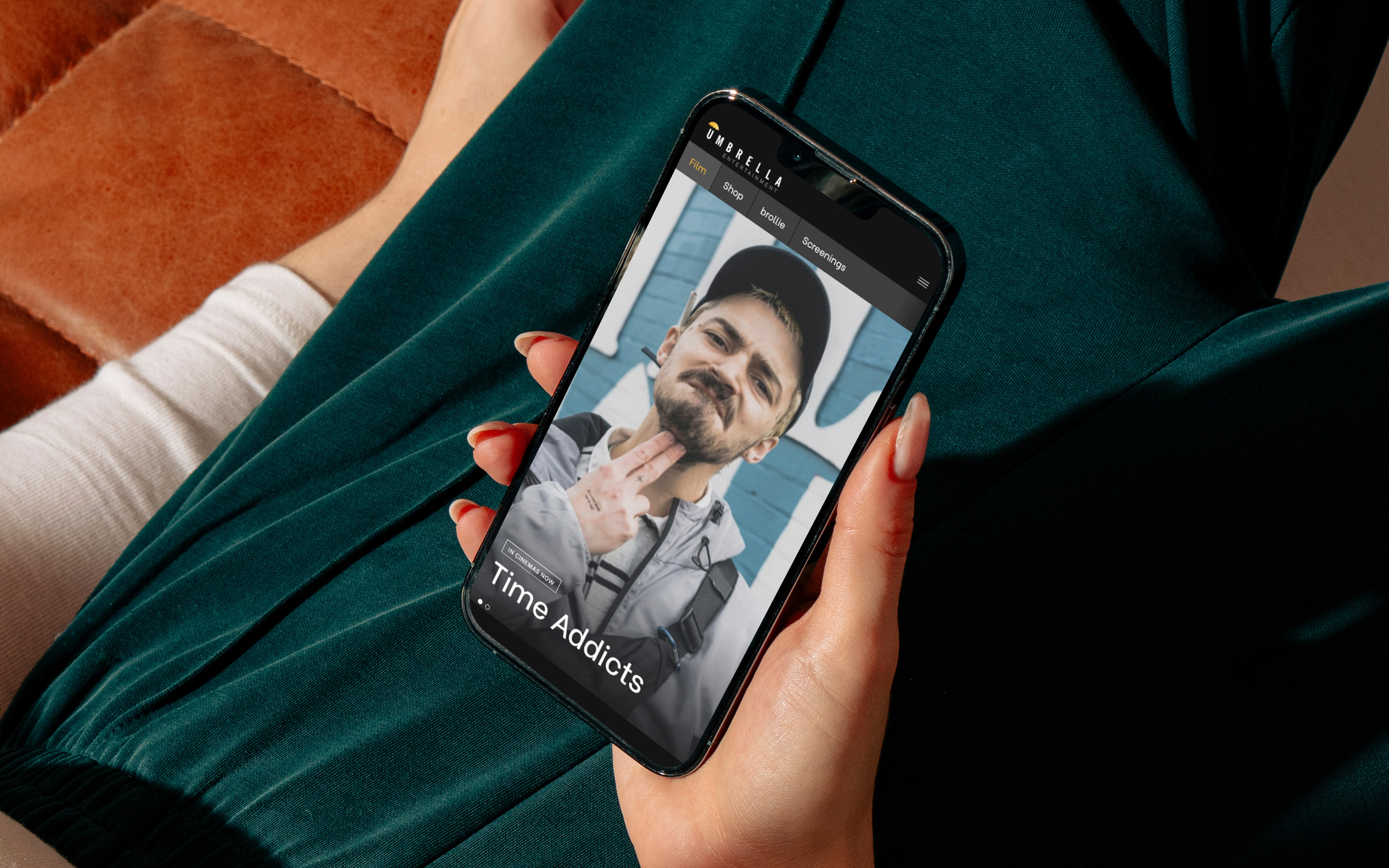 Close up of the Umbrella Entertainment website shown on a smartphone held by a woman wearing green pants.