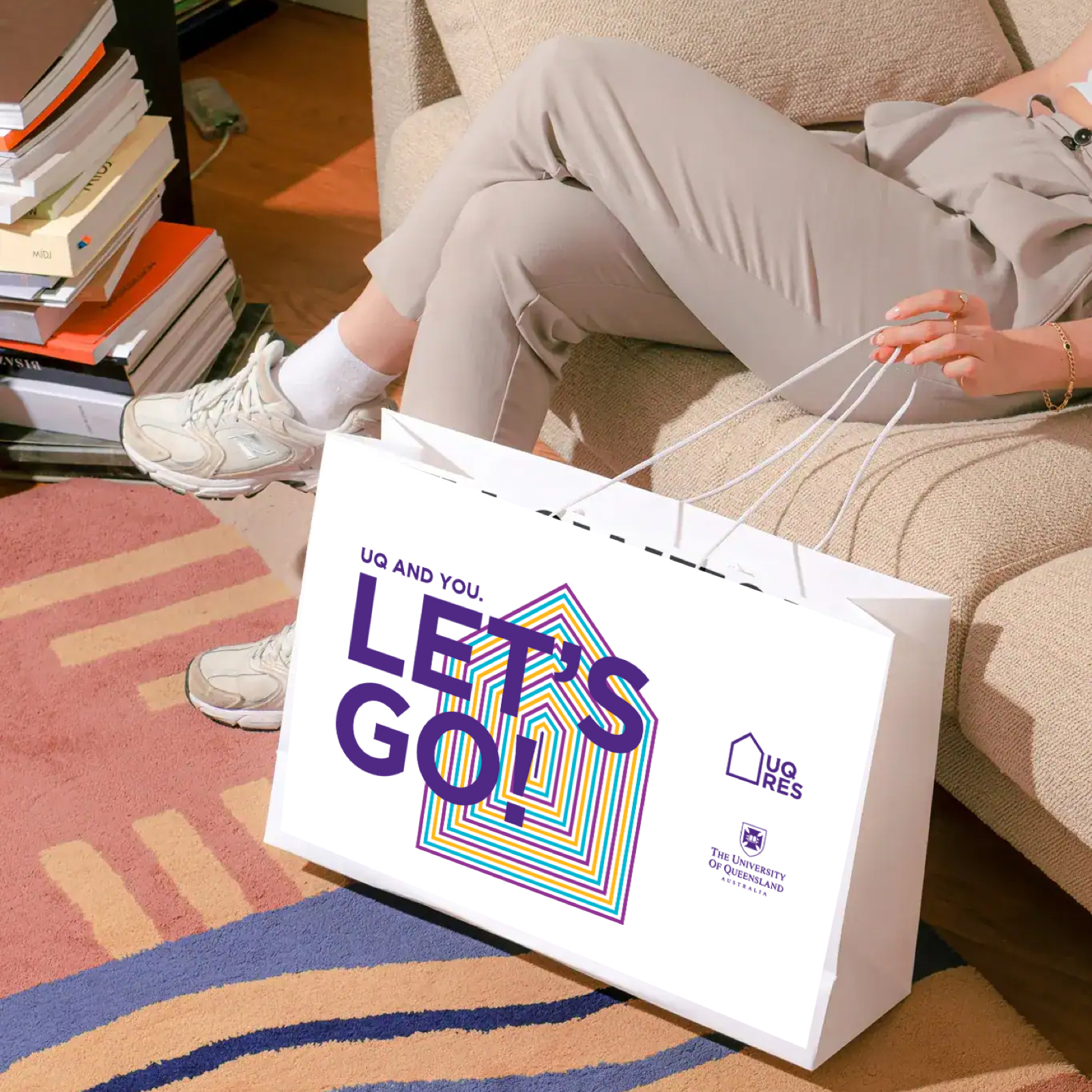 White bag with UQ branded graphics on it which read "Let's Go!" in large letters, concentric houses in multiple colours, and the UQ Res and University of Queensland logos.