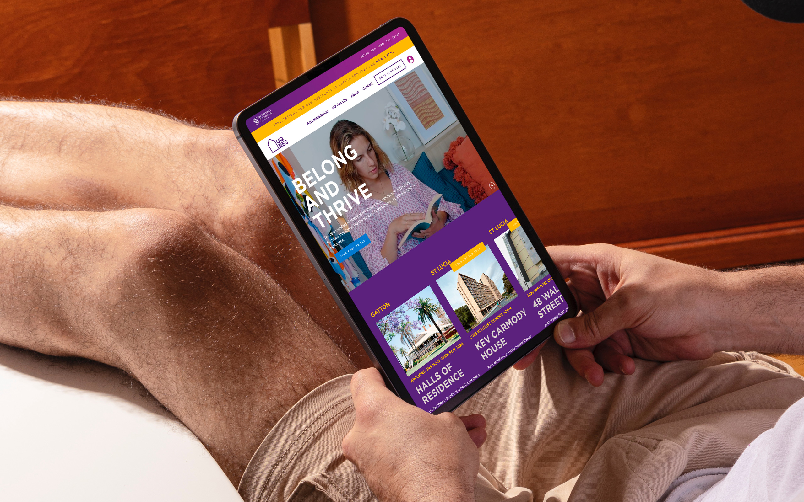 UQ Res website home page shown on a tablet being held by a man wearing tan shorts.