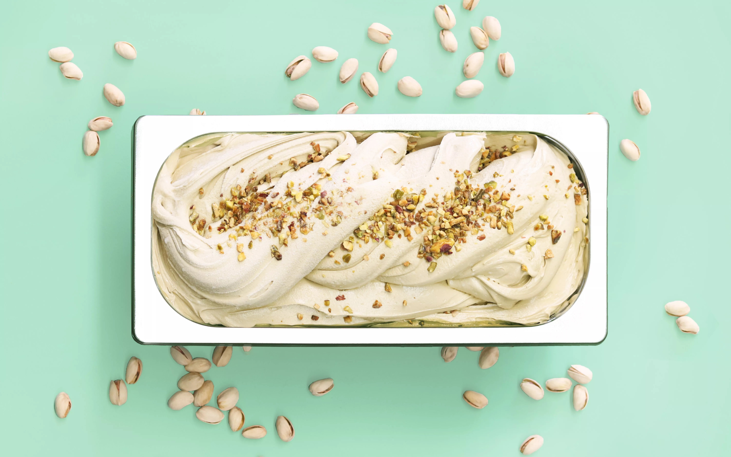 Full tub of pistachio gelato, surrounded pistachio nut shells.