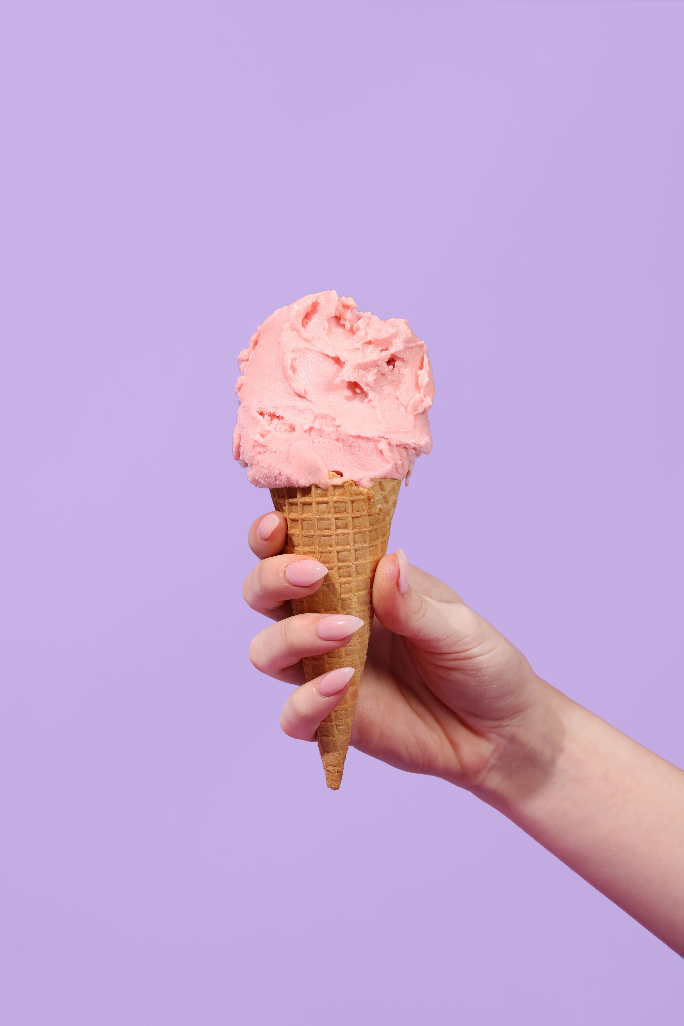 A cone of watermelon gelato held by a hand on a purple background.