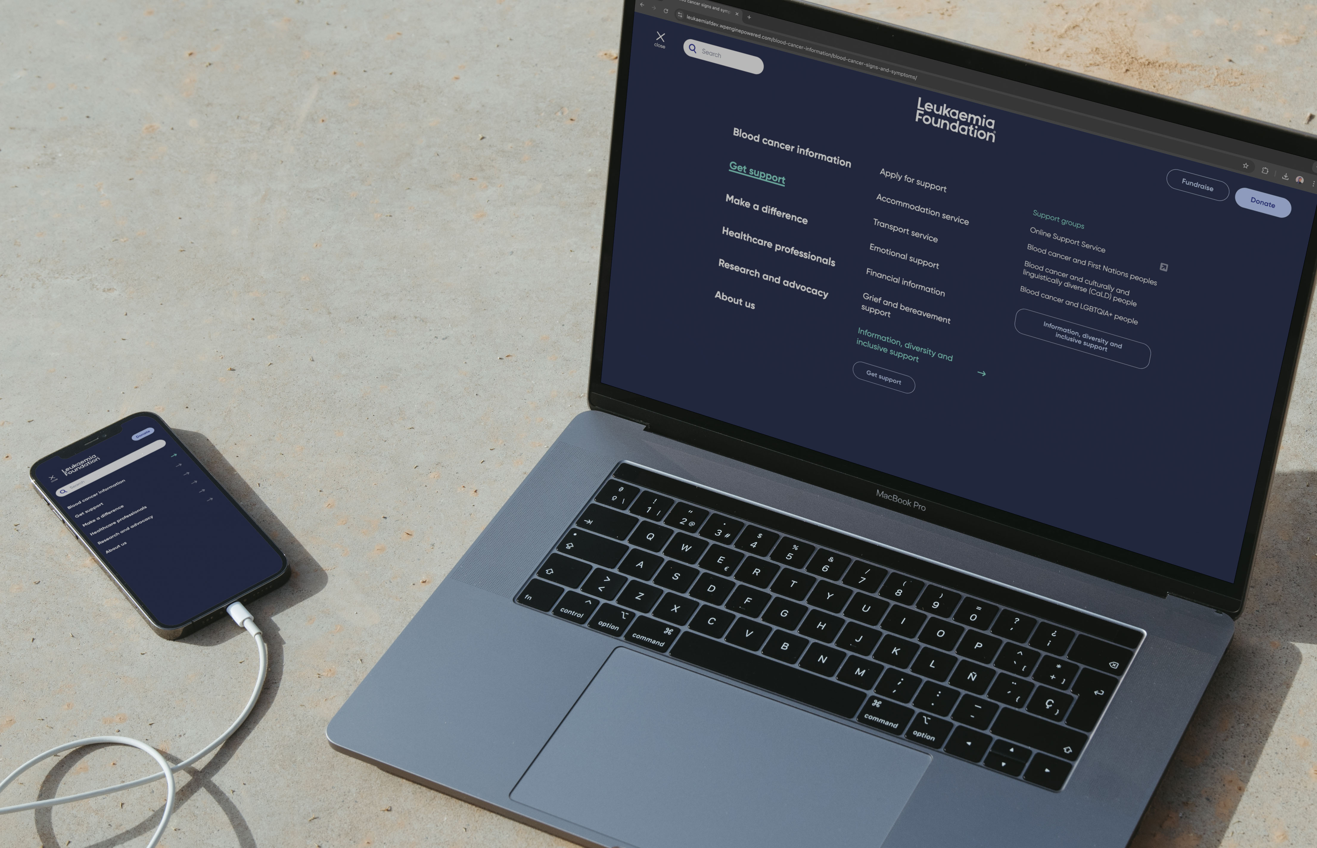 Leukaemia website mega menu shown on side-by-side laptop and phone, sitting on a beige floor.