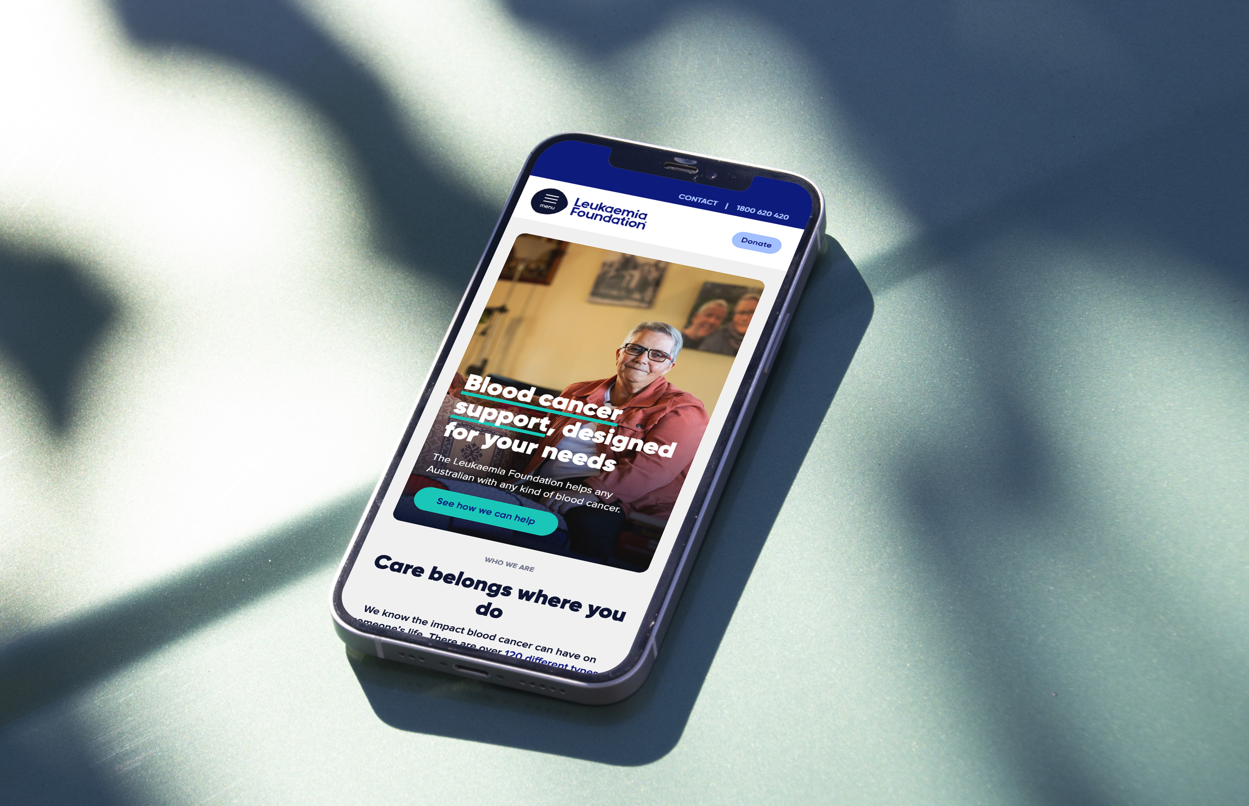 The Leukaemia Foundation website home page shown on a smartphone laying on a teal surface under some shadows.