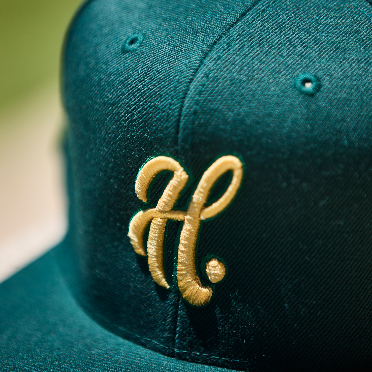 Close up detail shot of yellow Haskell logo on a dark green baseball cap.