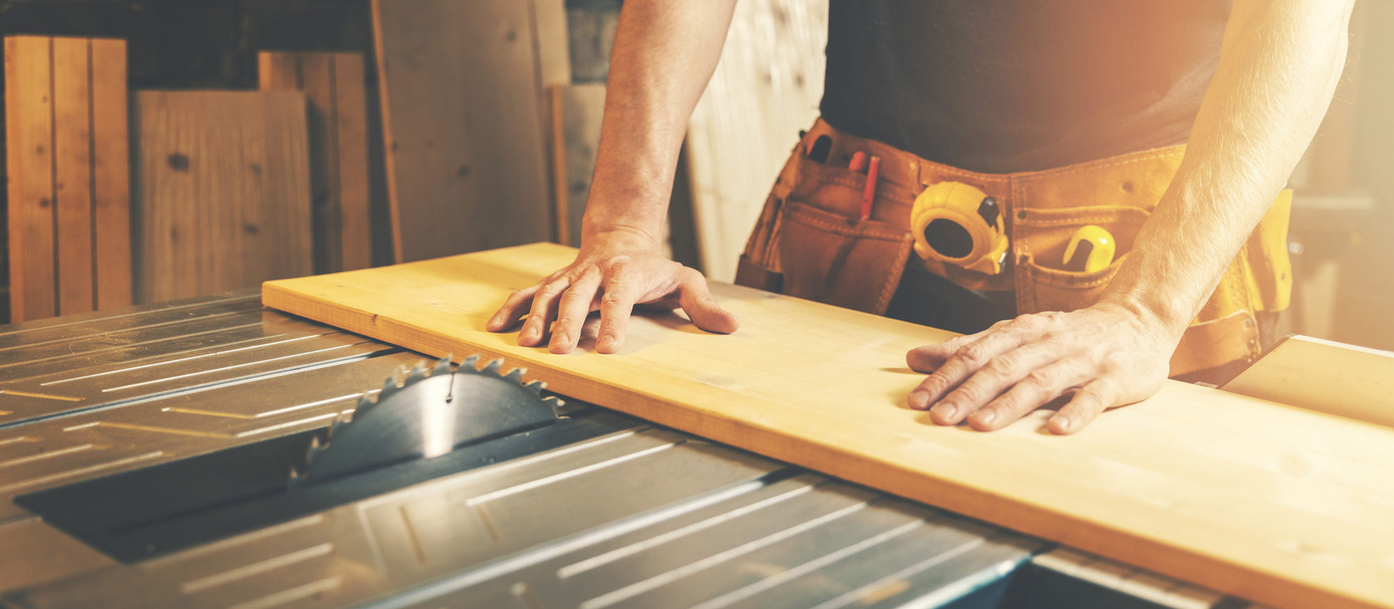 Man pushing large, flat piece of timber towards a table saw in a woodworking workshop.