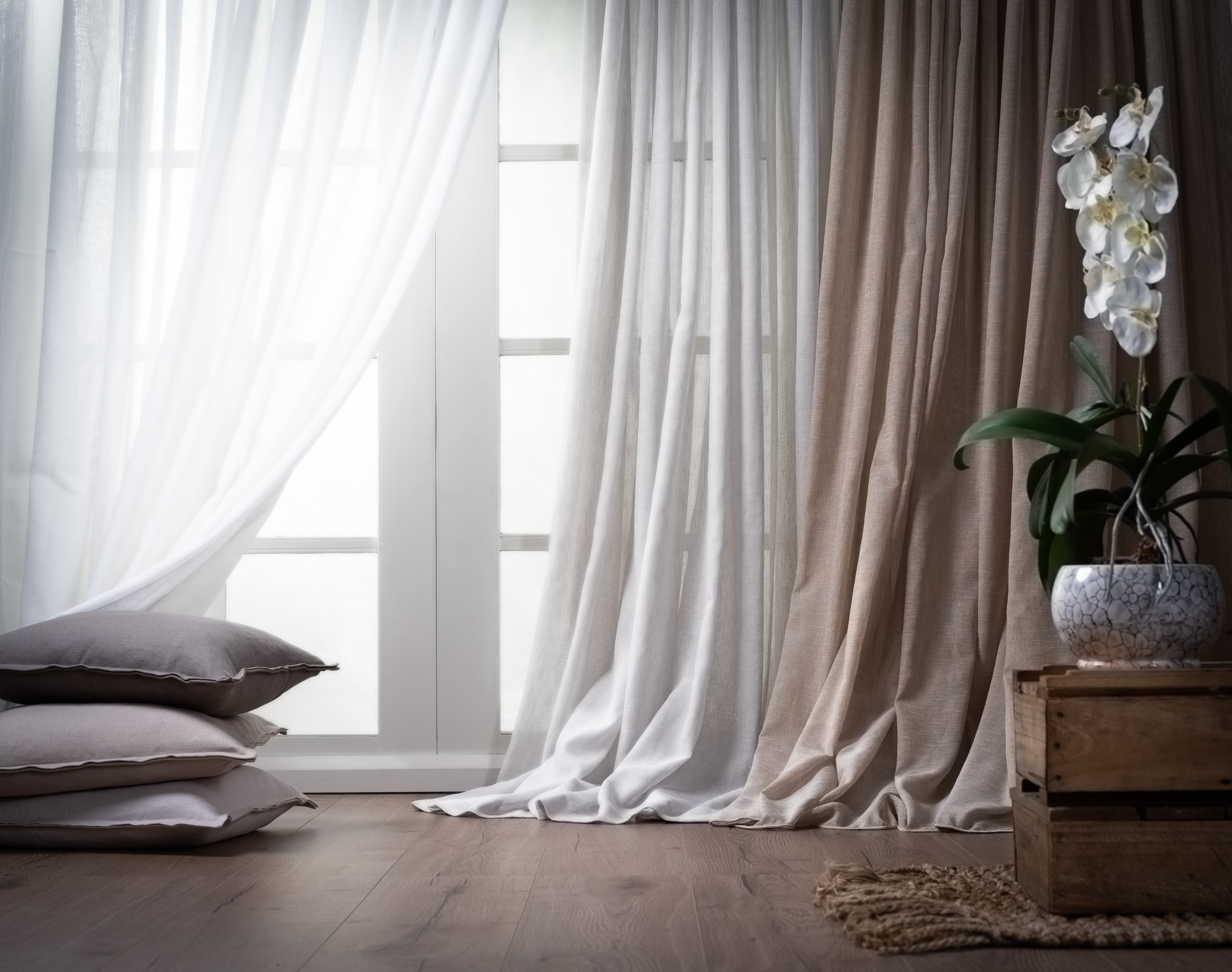 A white and tan curtain are draped across a hardwood floor.