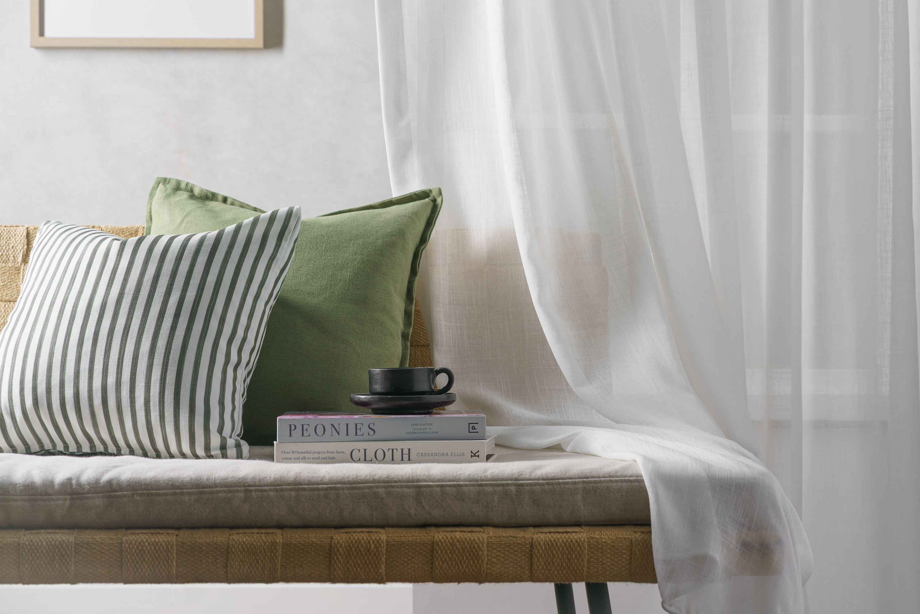 Fabric chair with white textile tastefully draped across it. There are also two pillows, two books and a teacup laid on the chair.
