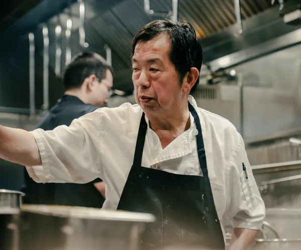 Middle-aged chef wearing a white coat and black apron working in a professional kitchen.