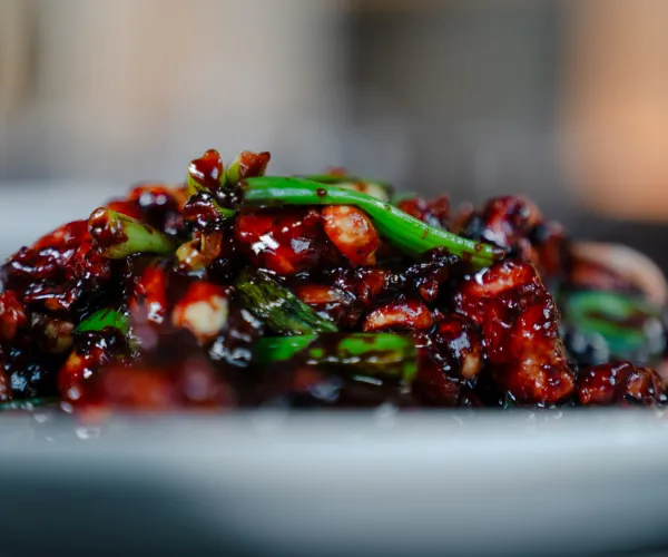 Close-up of stir-fried dish with dark sauce, green vegetables, and chopped meat on a plate.