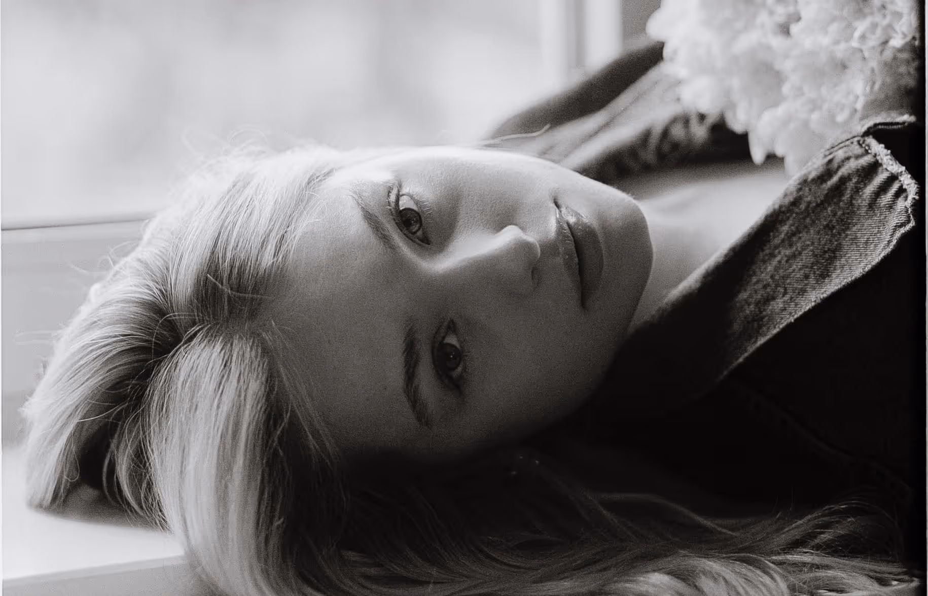 Black and white close-up of a woman lying down with her head resting sideways, looking softly at the camera.