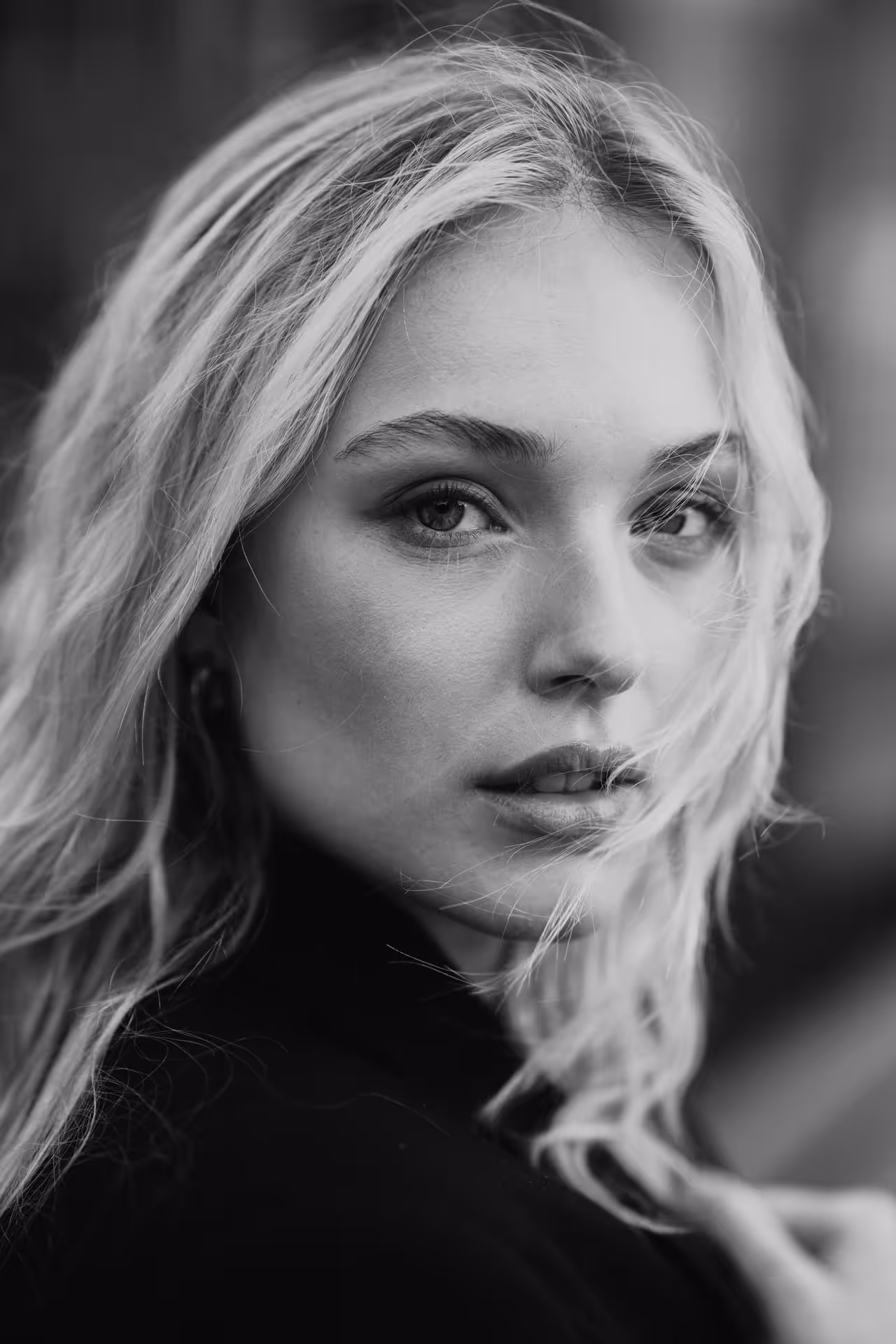 Close-up black and white portrait of a woman with wavy hair partially covering her face, looking directly at the camera.