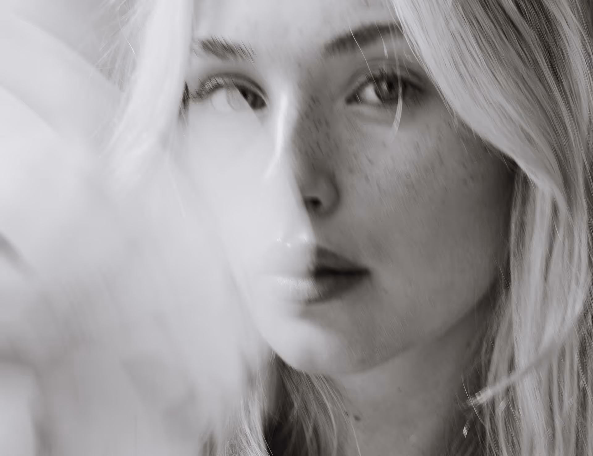 Close-up black and white portrait of a woman with light hair and freckles, partly obscured by a soft translucent fabric.